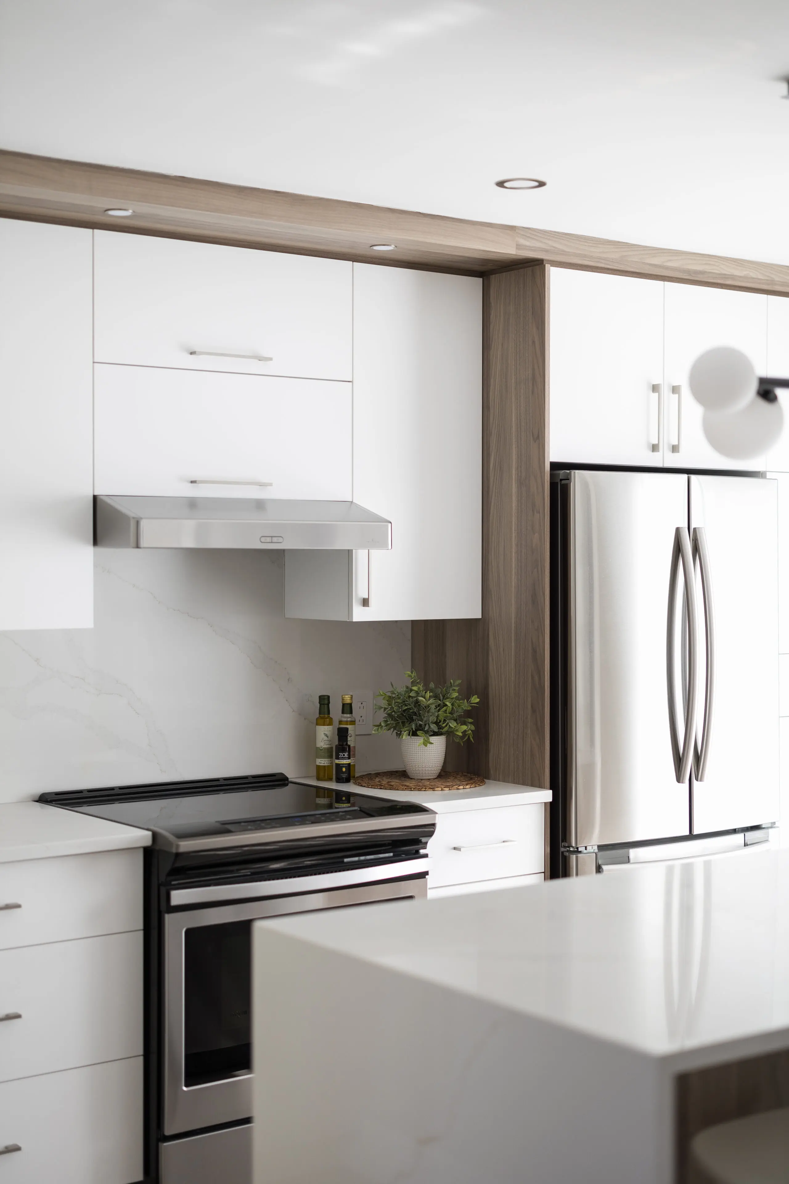 Cuisine moderne avec des armoires blanches, des appareils en acier inoxydable comprenant un réfrigérateur et une cuisinière, des comptoirs en marbre, une petite plante en pot et des bouteilles sur le comptoir à côté de la cuisinière.