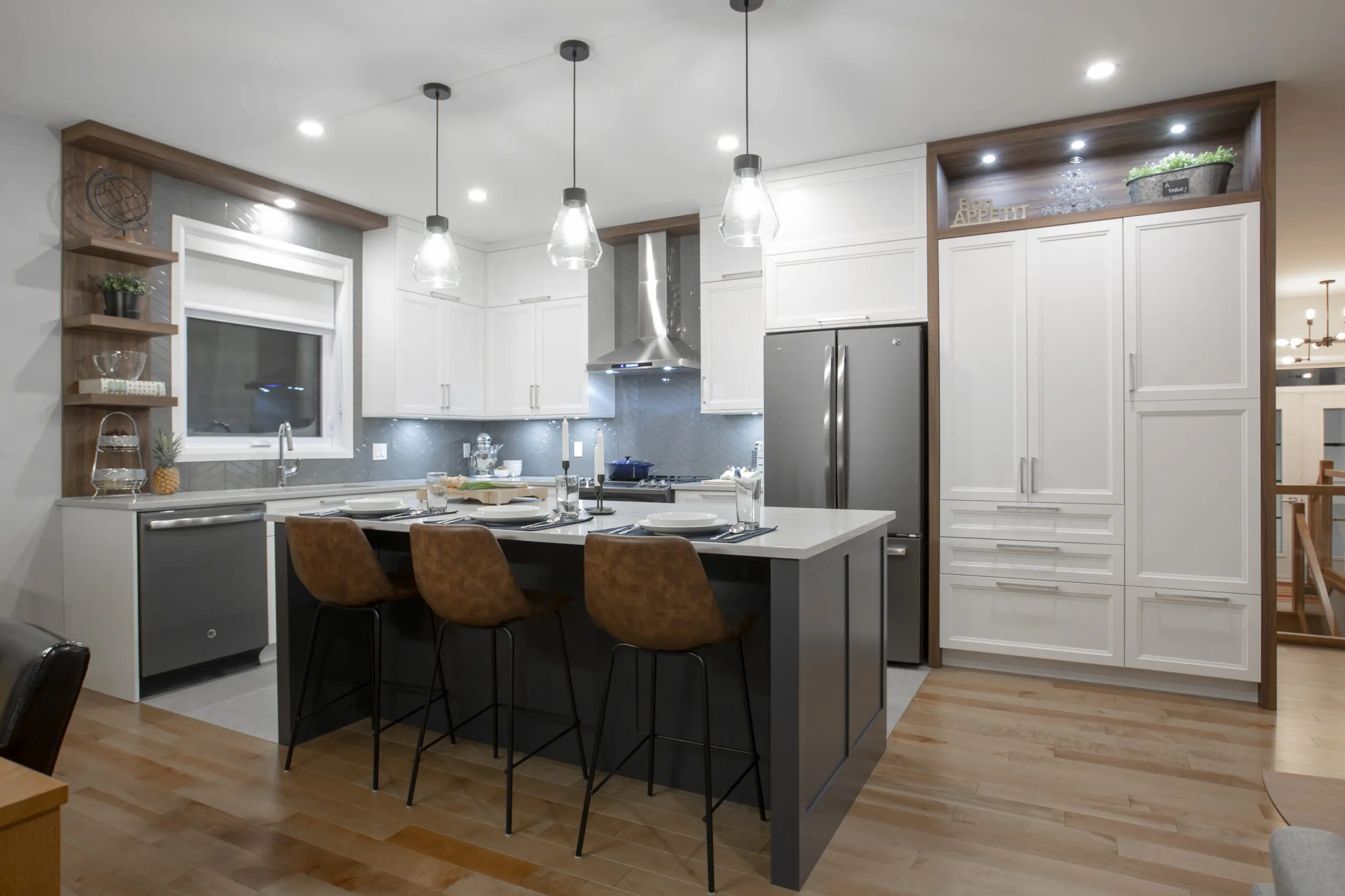 Cuisine moderne avec des armoires blanches, un îlot central avec trois tabourets de bar bruns, des lampes suspendues, des appareils électroménagers en acier inoxydable, des étagères ouvertes et des accents en bois sur un sol en bois dur clair.