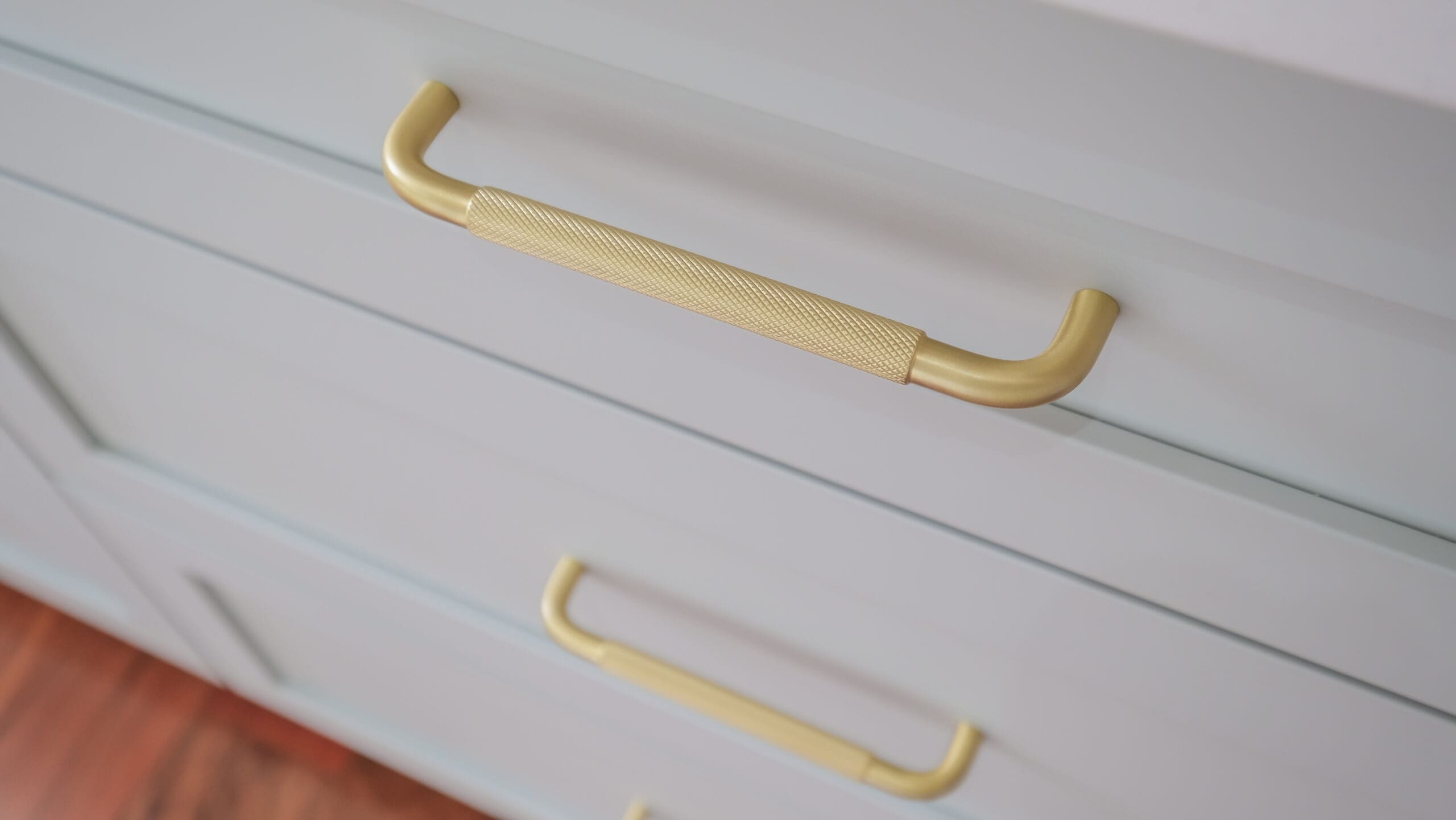 Gros plan sur des tiroirs modernes gris clair avec des poignées en métal doré, au design texturé. Les tiroirs font partie d'une armoire ou d'une commode, et les poignées ont un aspect élégant et contemporain.