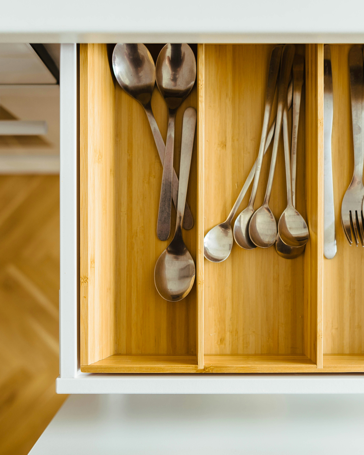 Un tiroir de cuisine ouvert avec un organisateur en bambou contenant de grandes cuillères, de petites cuillères et quelques fourchettes, chacune soigneusement rangée dans des sections séparées. La surface est propre et organisée.