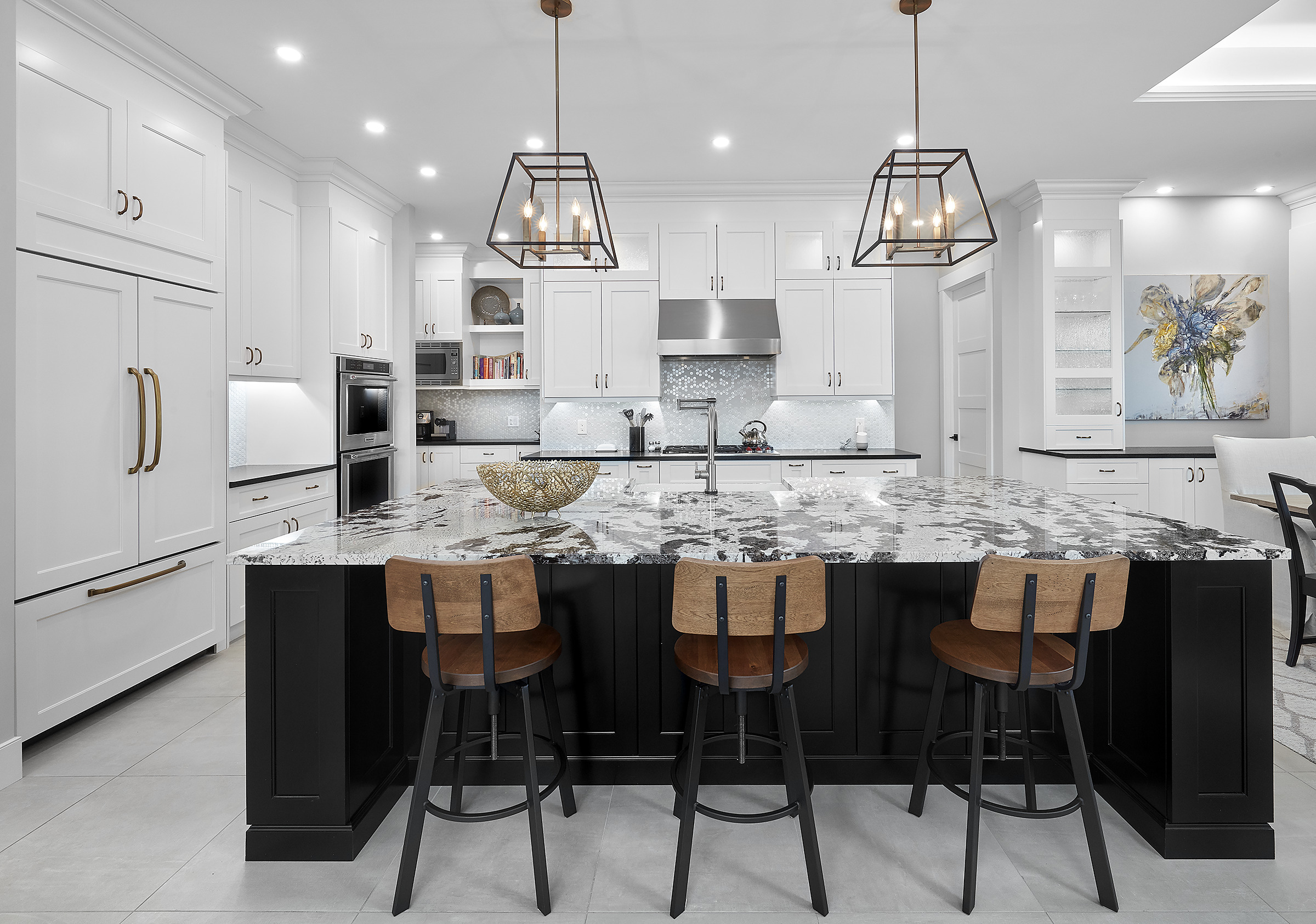 Cuisine moderne avec des armoires blanches, un grand îlot en marbre noir et blanc avec trois tabourets de bar en bois, des lampes suspendues au plafond, des appareils en acier inoxydable et des œuvres d'art décoratives au mur.
