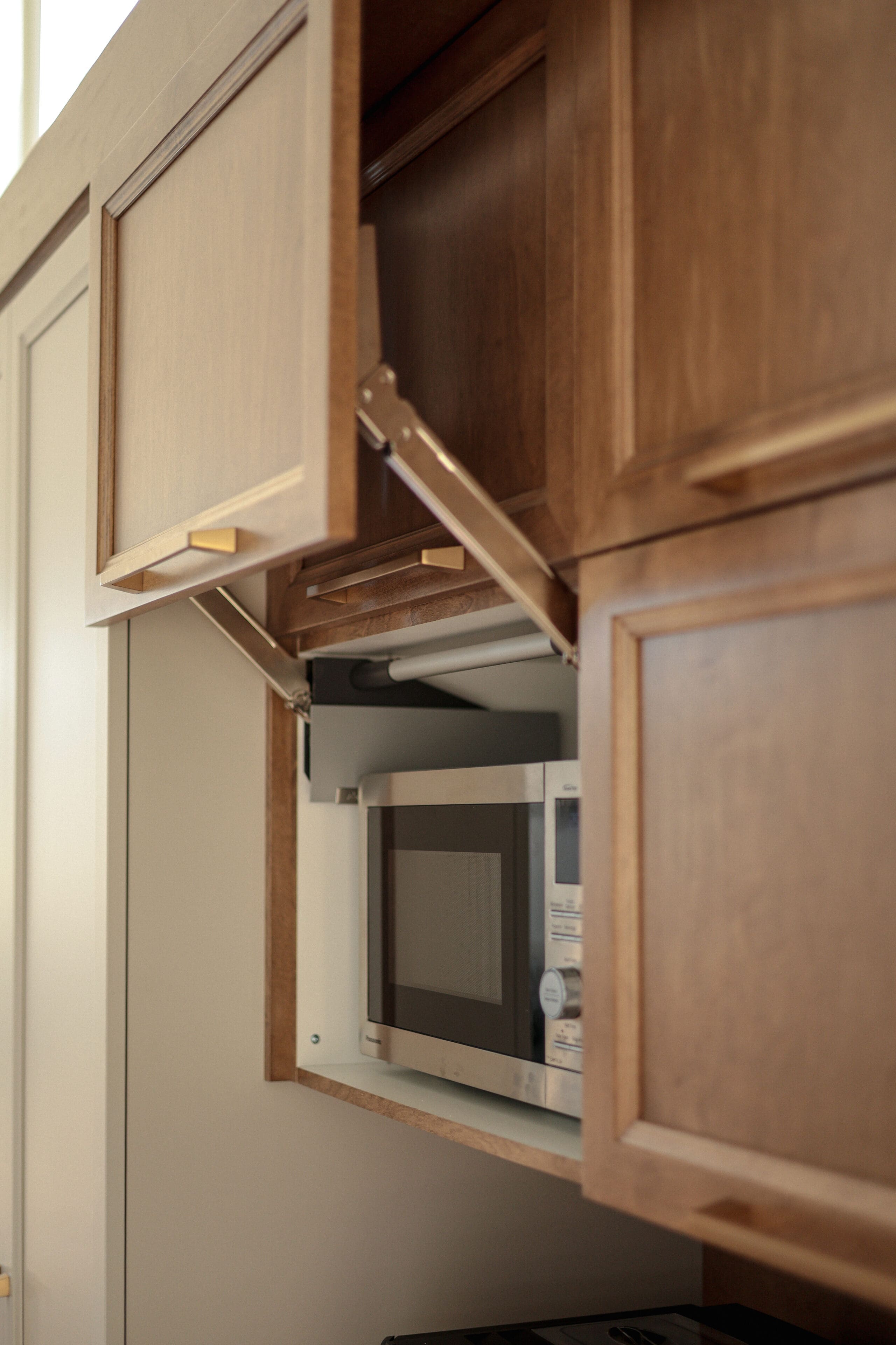Un four à micro-ondes est encastré dans un meuble de cuisine aux portes en bois, dont l'une s'ouvre à l'aide d'une charnière, laissant apparaître l'appareil à l'intérieur.