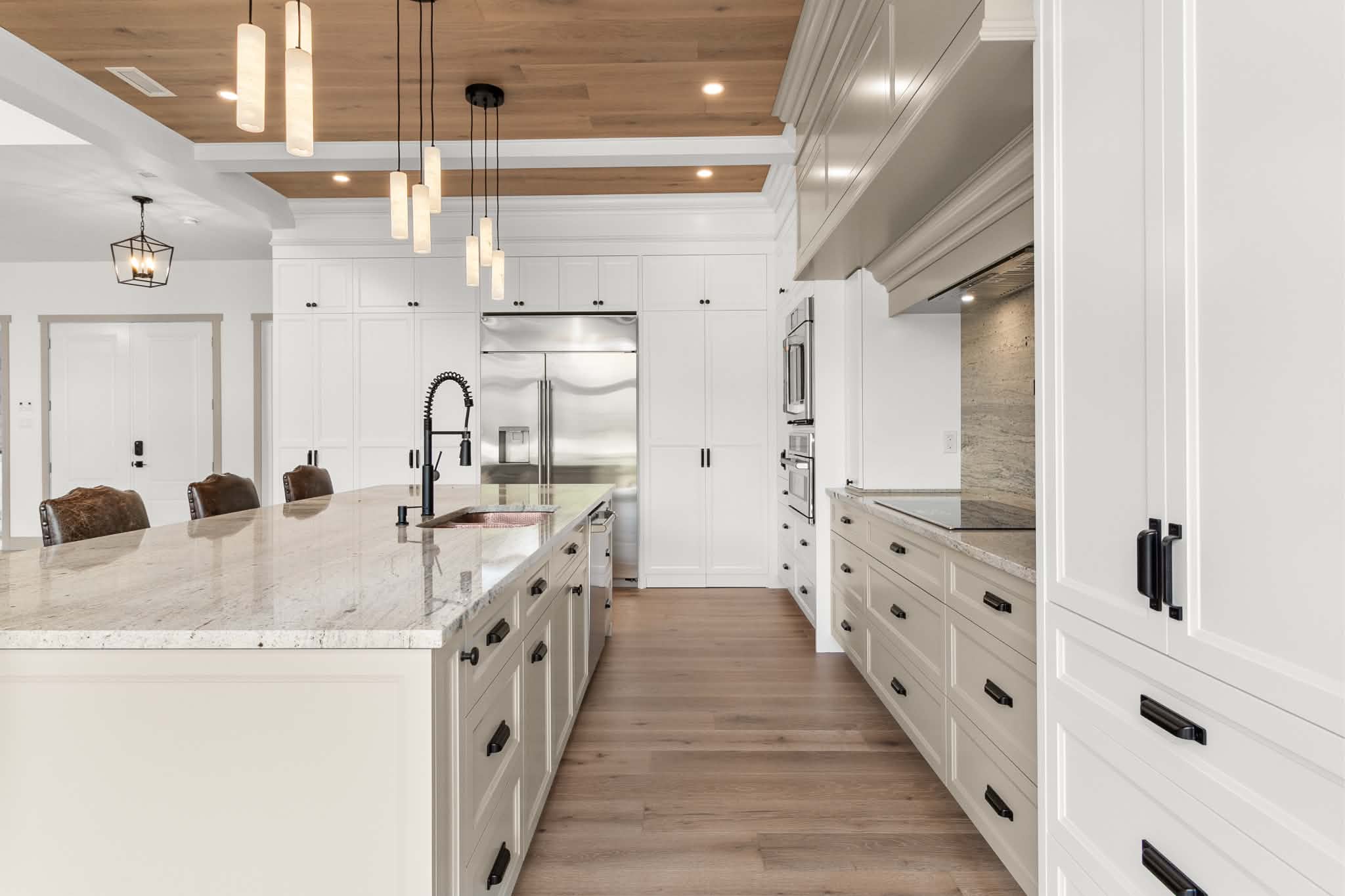 Cuisine moderne avec des placards blancs, des appareils électroménagers en inox, un grand îlot en marbre doté d'un robinet noir, des suspensions et un parquet clair. L'espace est lumineux et spacieux, avec des tons neutres et épurés.